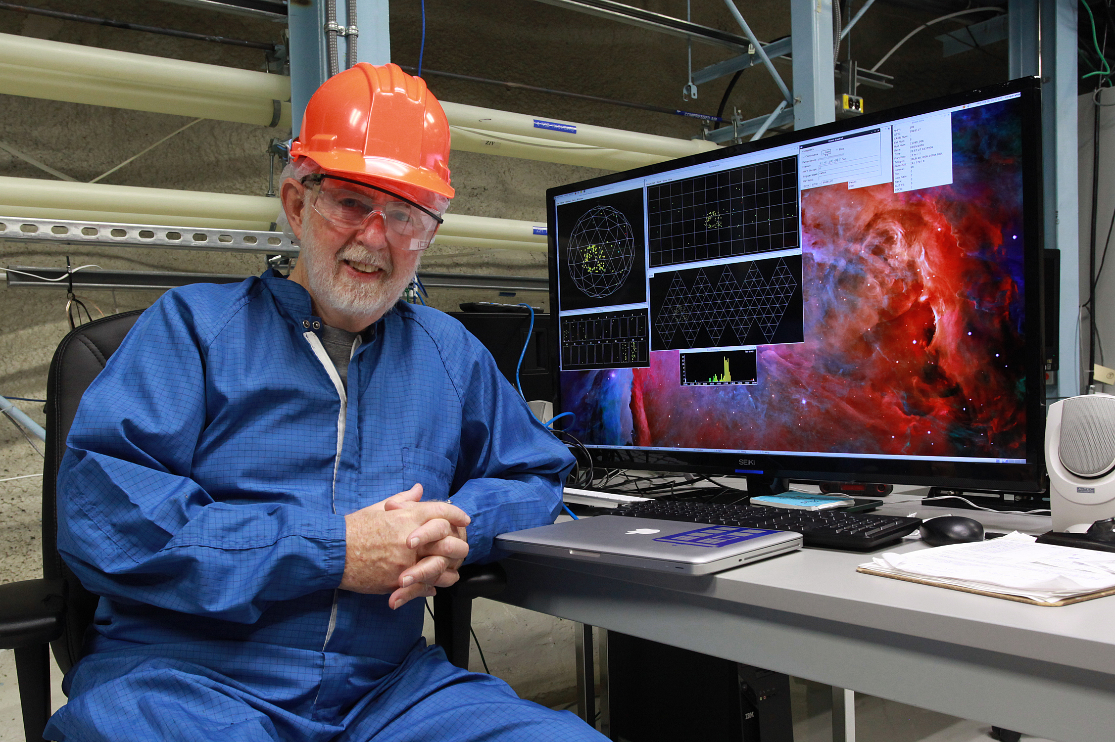 Arthur B. McDonald with a hard hat on, sitting in front of his computer