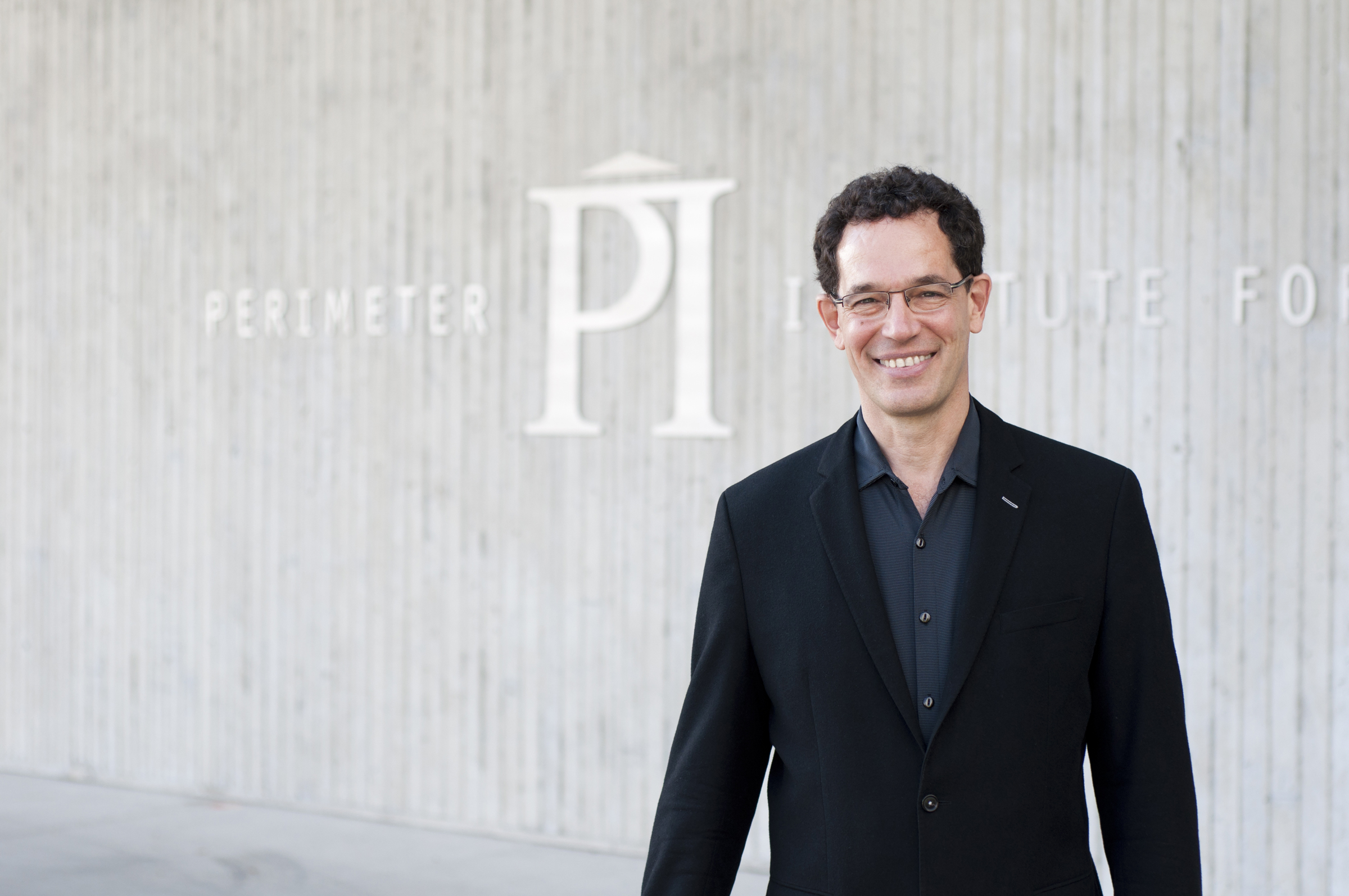 Portrait of Neil Turok standing in front of Perimeter Institute's building facade