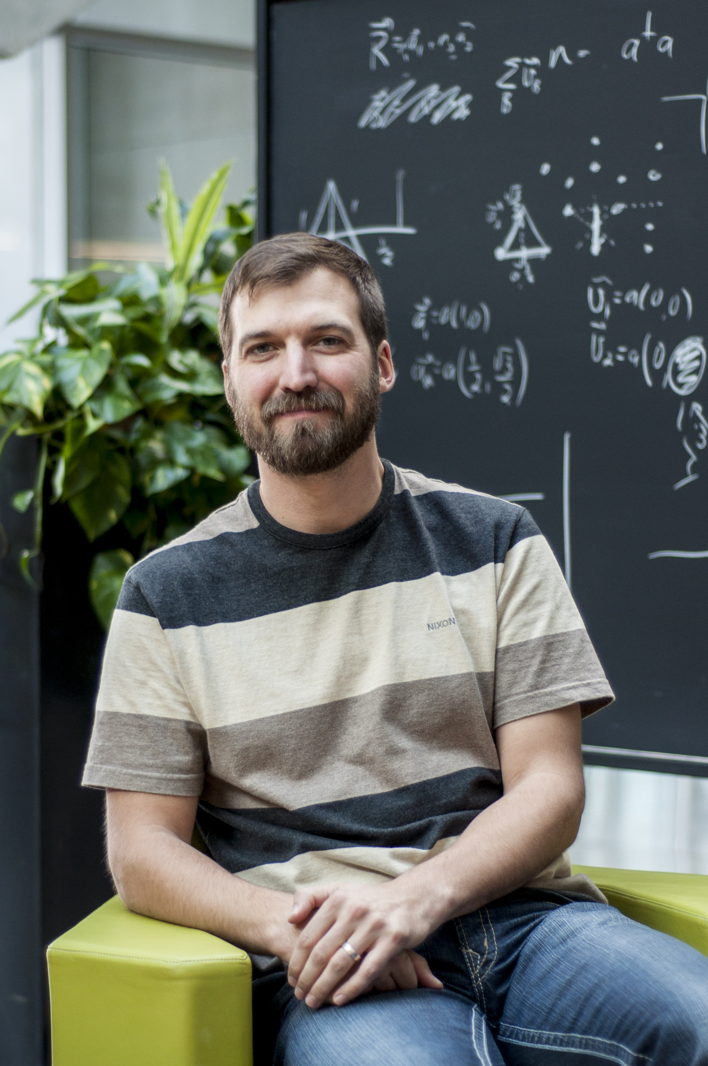 Portrait of Roger Melko in front of a blackboard in the atrium at perimeter institute