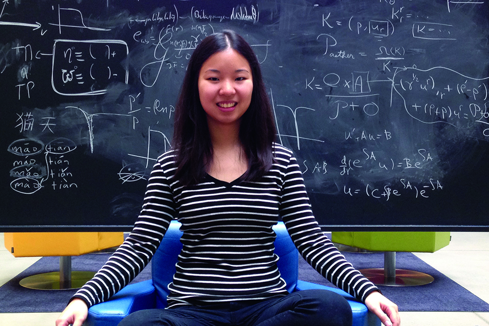 Woman sitting cross-legged on a chair in front of a blackboard