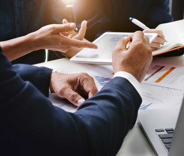 Close up of men and women's hands going over paperwork and a tablet of information