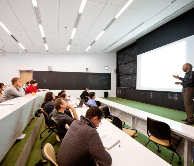 Man standing at the front of a lecture hall talking to people