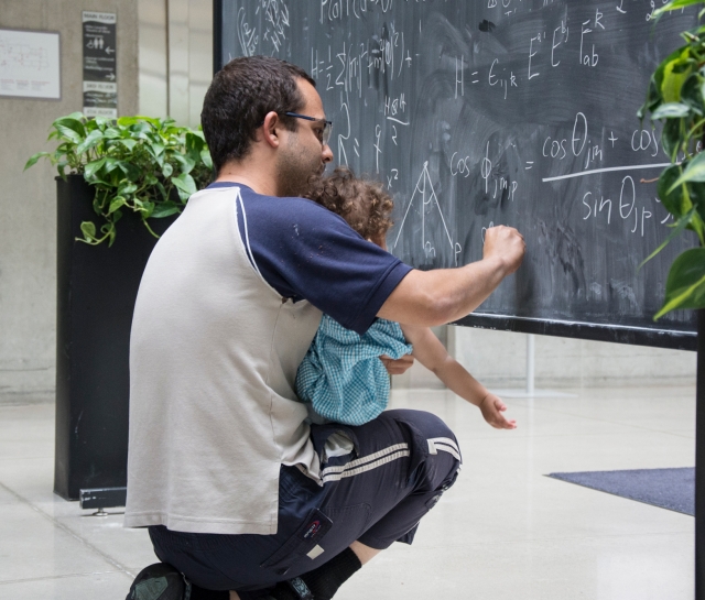 Man holding baby and writing equations on a blackboard