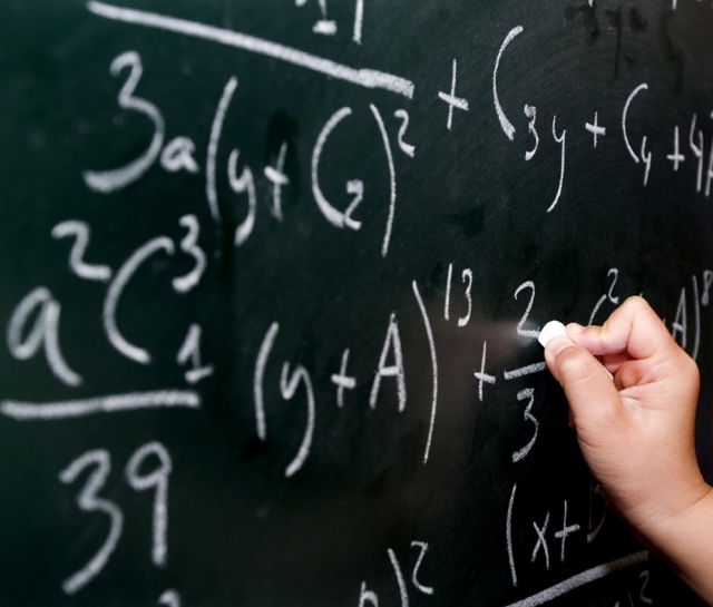 Picture of a hand writing equations on a blackboard