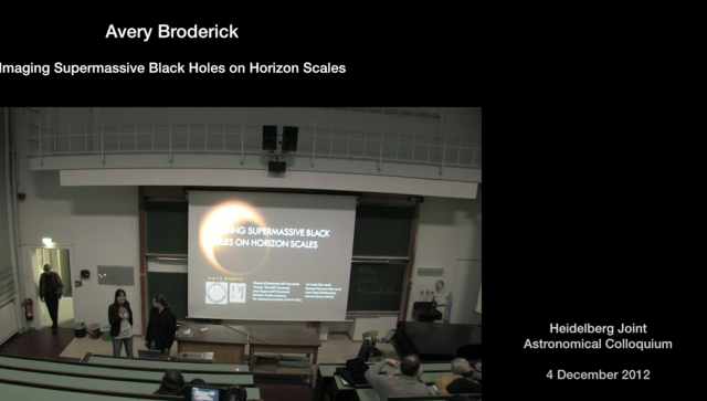 Man standing at the front of a lecture hall talking to people