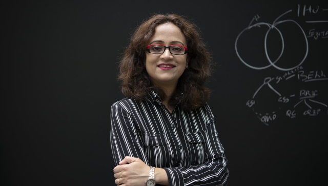 Woman with brown hair and glasses standing in front of a blackboard of equations