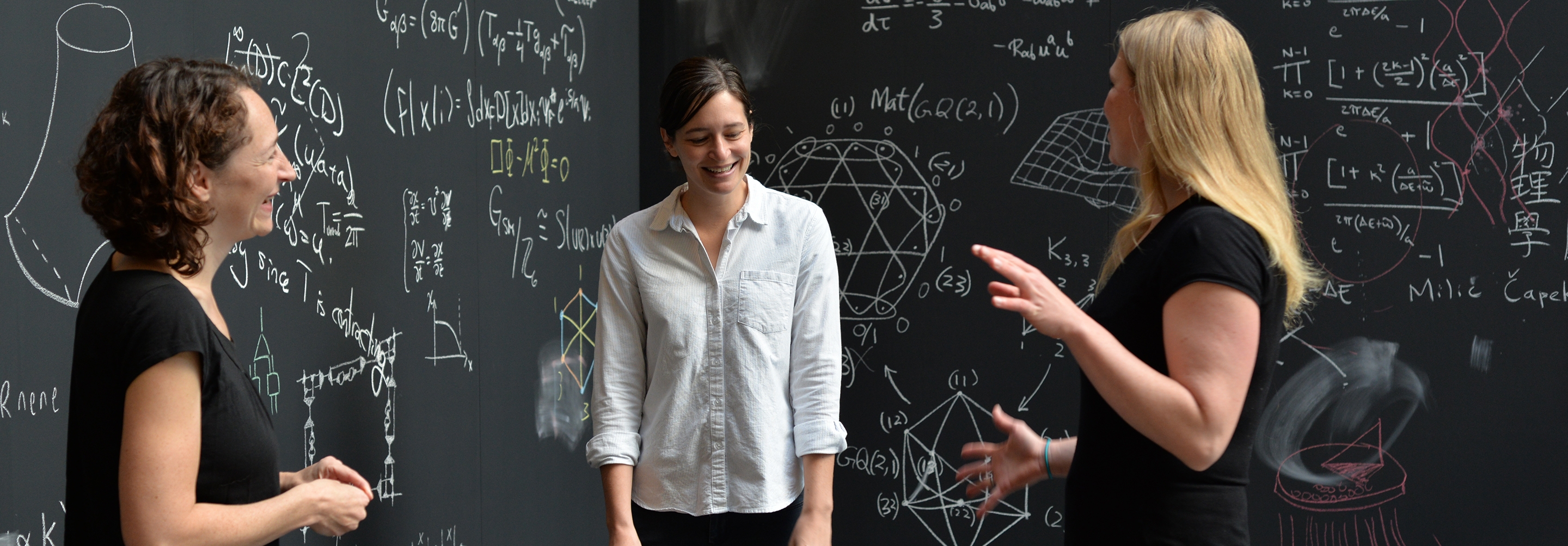 Three women surrounded by chalkboards with equations