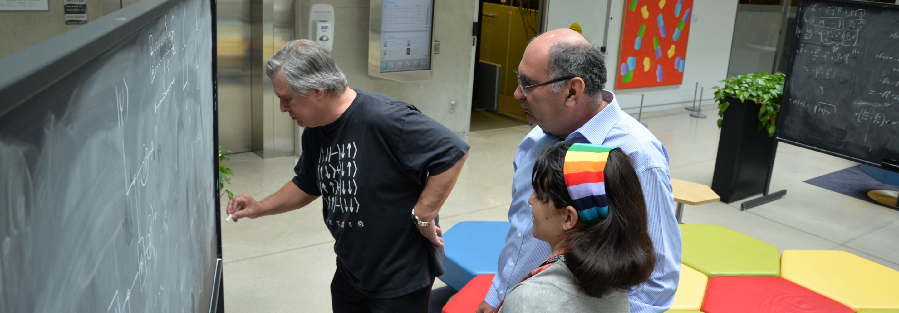 Two men and a woman collaborating at a chalkboard in atrium