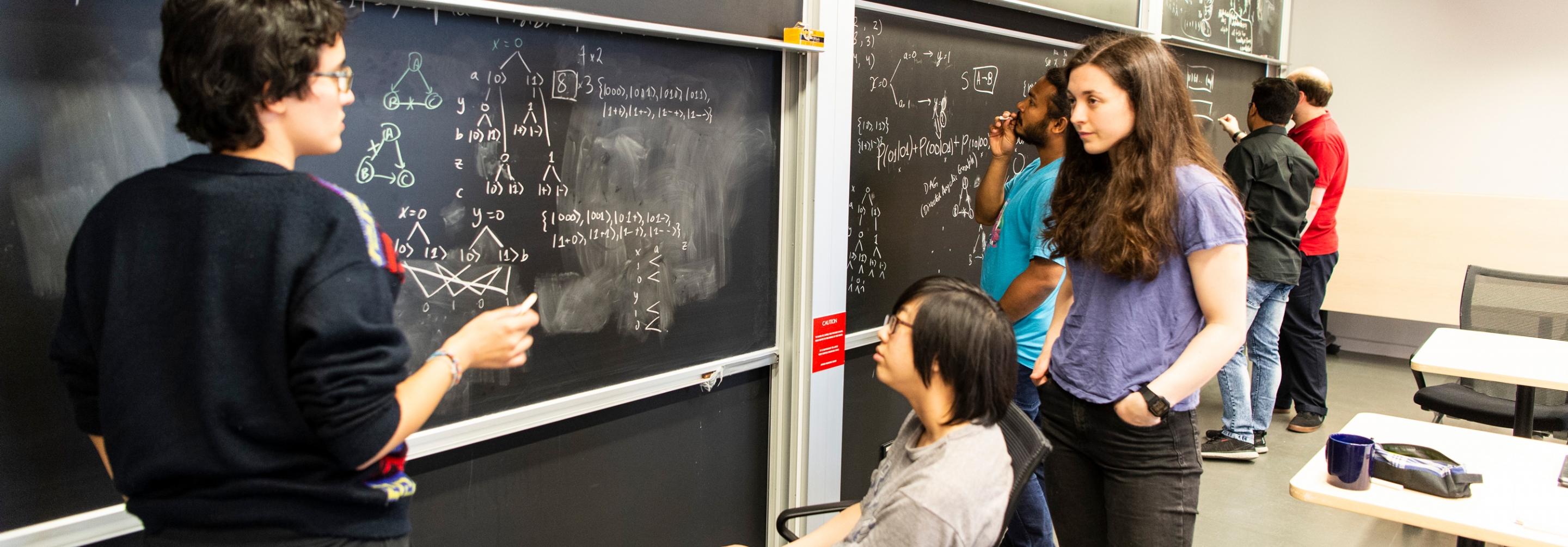 Group of grad students collaborating at blackboards together