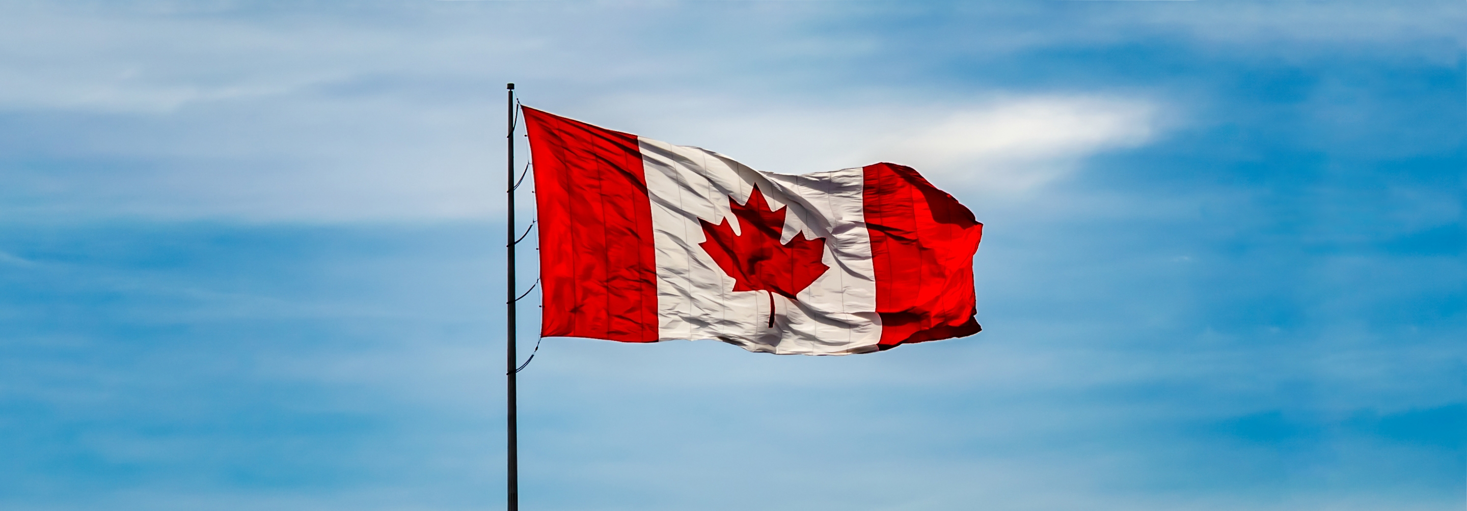 Canada flag flying with a blue cloudy sky behind it