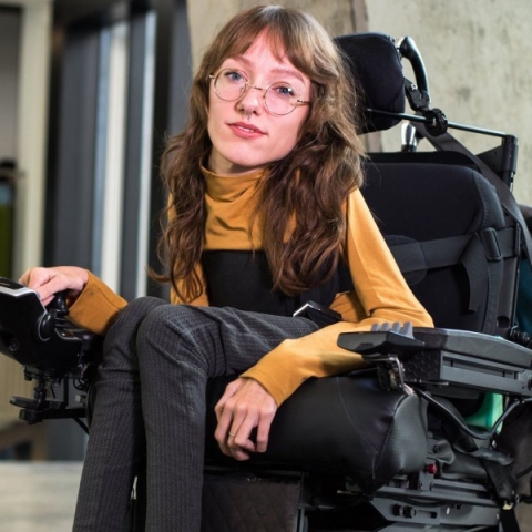 Woman in yellow shirt and grey pants sitting in a motorized wheelchair