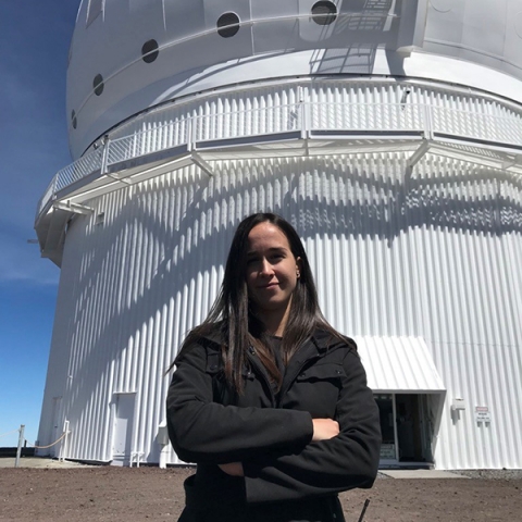 Woman wearing a black coat standing outside in front of a white telescope