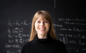 Portrait of Christine Muschik in front of a blackboard of equations