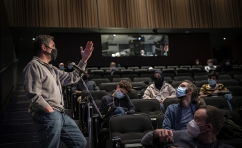 Man standing in front of a group of people in a theatre talking