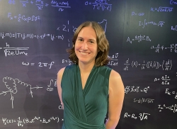 Woman wearing a green shirt standing in front of a blackboard of equations